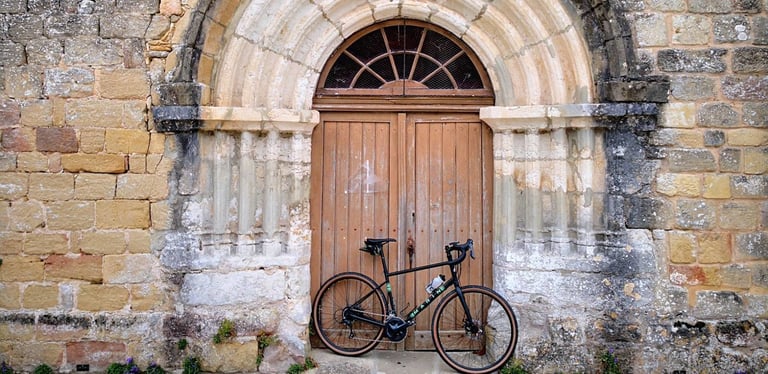 Marin Four Corners leaning against the arched wooden door of an old stone building.