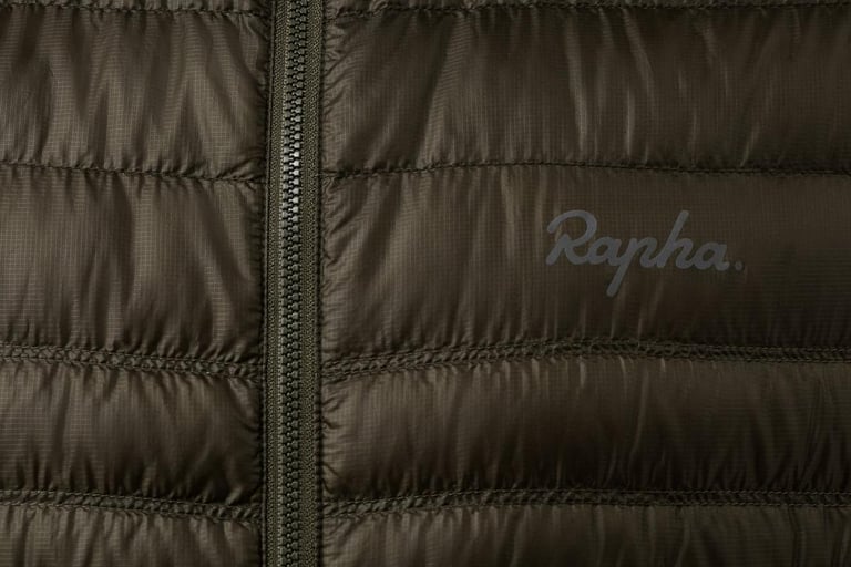 Rapha Explore down jacket in olive, close-up of the quilted baffles, front zip and logo.