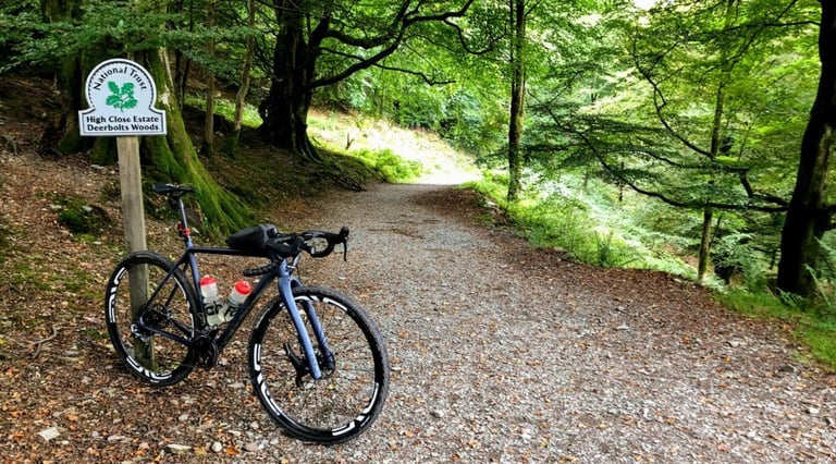 Lauf True Grit beside a National Trust sign for Deerbolts Woods on a gravel track in the Lake District.