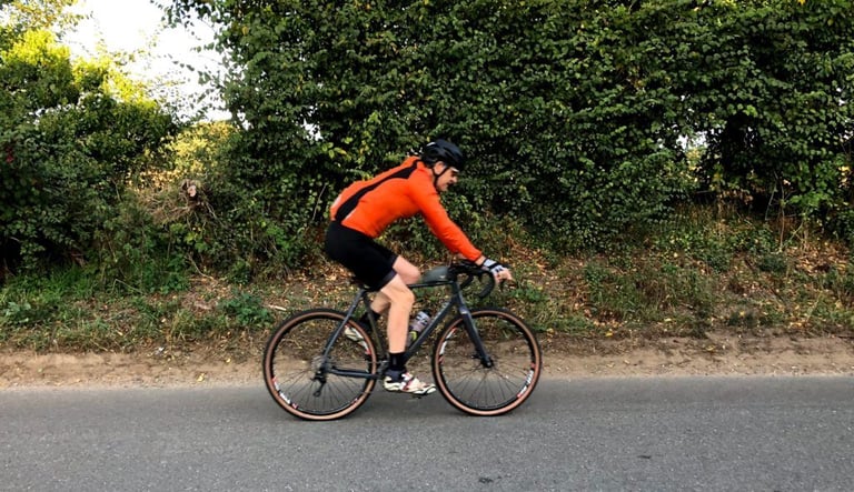 Side view of a rider in the Galibier VentUltra jacket, showing the waist-length hem, beside a hedge.