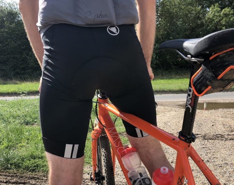Rear view of a rider in Endura FS260-Pro bibshorts astride an orange bike, reflective double stripes on each leg hem.