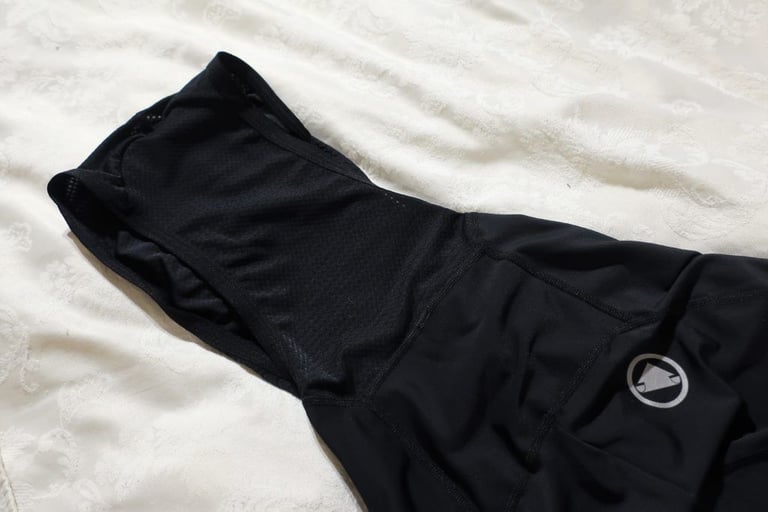 Enclosed mesh-backed straps of Endura FS260-Pro bibshorts with a grey logo on the rear panel, laid on a bedspread.