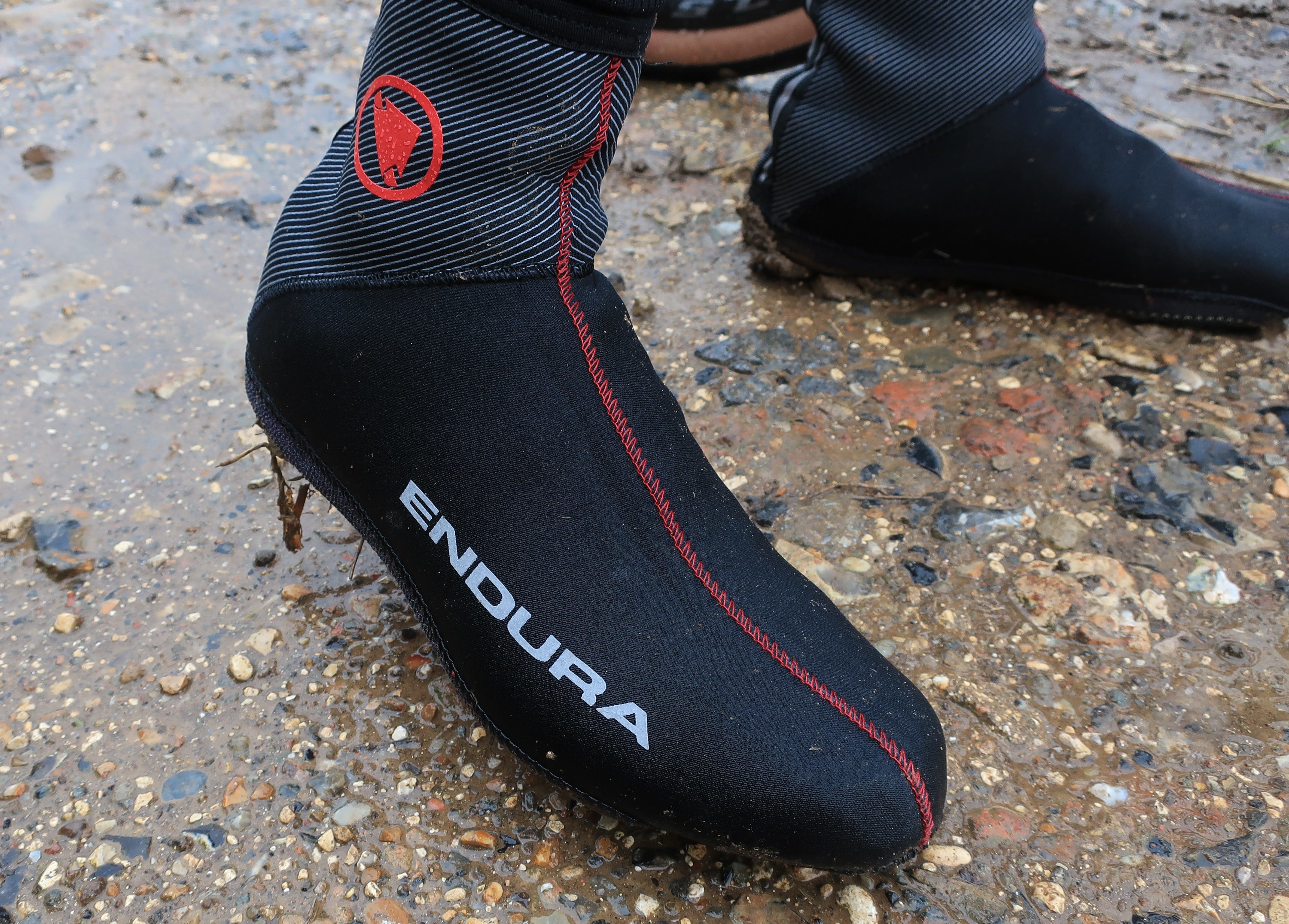 Side view of the neoprene Endura Freezing Point overshoe with red stitching and the logo on wet gravel.