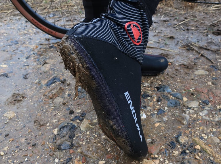 Muddy toe of an Endura Freezing Point overshoe on a wet gravel track, the aramid sole edge frayed with grit.