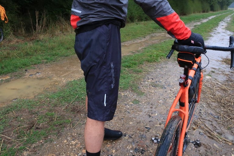 Front view of the Endura MTR Waterproof Shorts with reflective tab and logo, worn beside a puddled track.