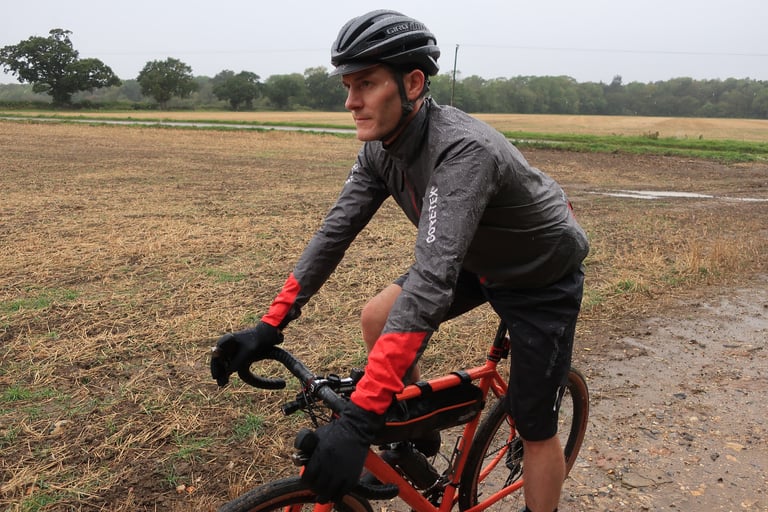Rider in the Gore C5 Shakedry 1985 Viz jacket on a gravel bike beside a stubble field in the rain.