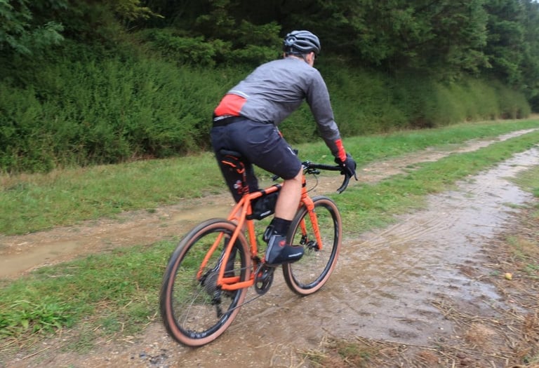 Rider heads away along a wet track wearing the Endura MTR Waterproof Shorts and a grey rain jacket.