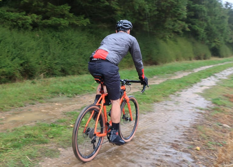 Rider seen from behind in the Gore Shakedry 1985 Viz jacket, riding a muddy gravel track in the rain.