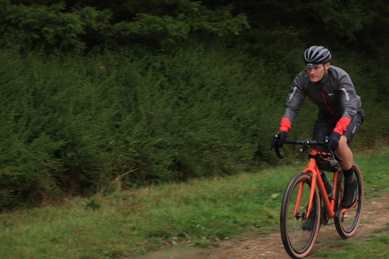 Rider in the Gore C5 Shakedry 1985 Viz jacket with red cuffs on an orange gravel bike, on a damp track.