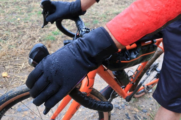 Rain-spotted Endura Pro SL Primaloft glove on the drop bars of an orange gravel bike fitted with a frame bag.