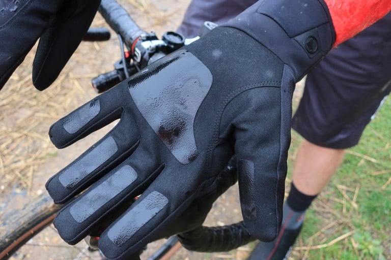 Wet palm of the Endura Pro SL Primaloft glove, with grip patches on the fingers, held beside a gravel bike's handlebar.