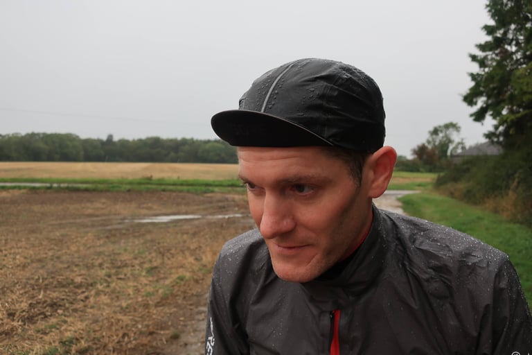 Rider wearing the Gore Shakedry Cap with the peak down beside a muddy field on a grey, wet day.
