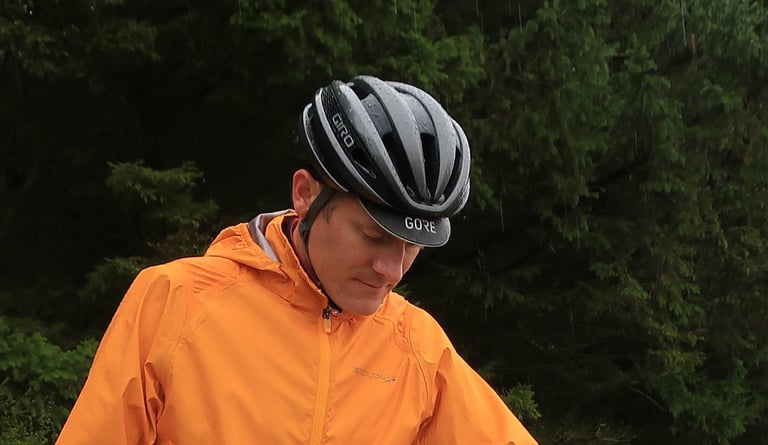 Gore Shakedry Cap peak showing under a Giro helmet on a rider in an orange jacket in the rain.