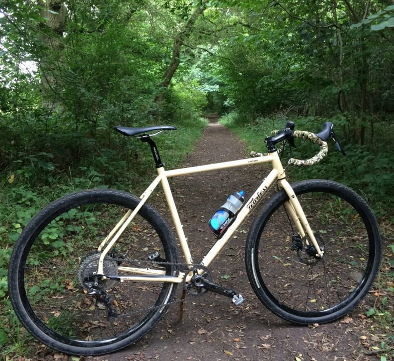 Fearless Vulture gravel bike on a leafy woodland path with green foliage overhead.