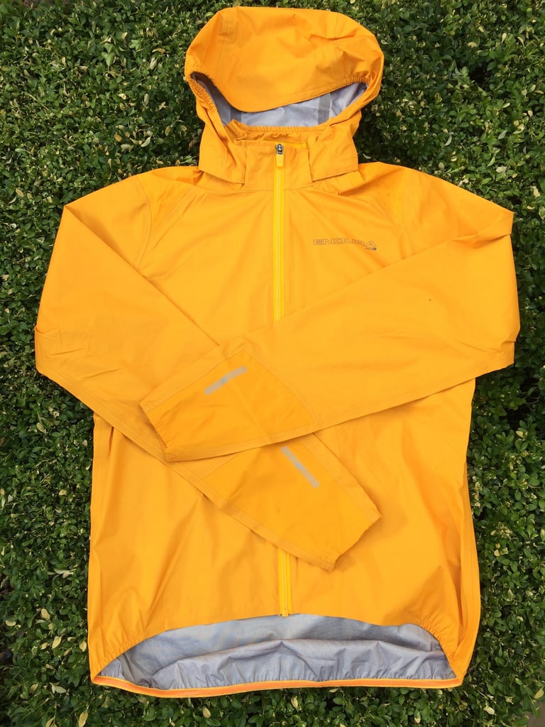 Endura MTR Shell Jacket laid flat on a hedge, showing the hood, full-length zip and reflective cuff strips.