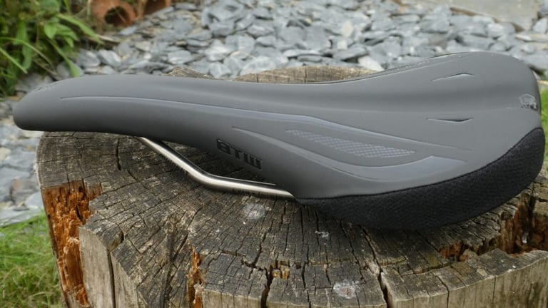WTB SL8 saddle in black with titanium rails, three-quarter view on a tree stump in front of slate chippings.