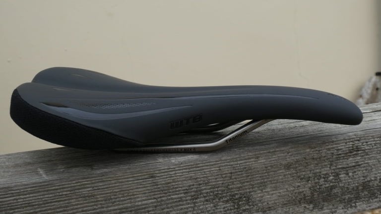 WTB SL8 saddle in profile on a weathered fence rail, showing its short dropped nose and titanium rails.