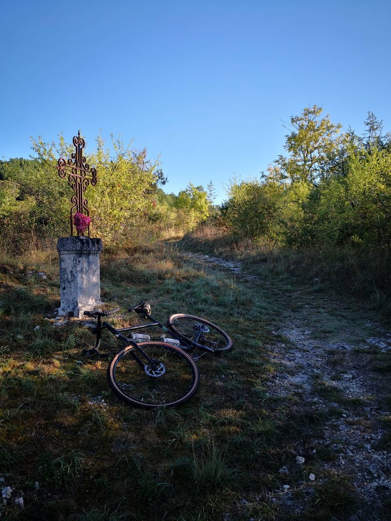 Marin Four Corners lying on a rough stony track beside a wrought-iron wayside cross on a stone plinth.