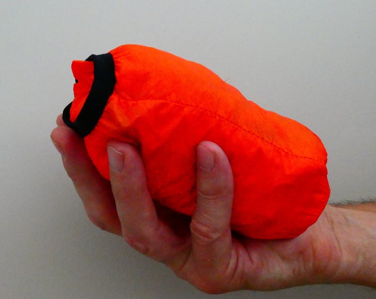 Galibier VentUltra jacket packed into its own small orange bag, held in one hand.