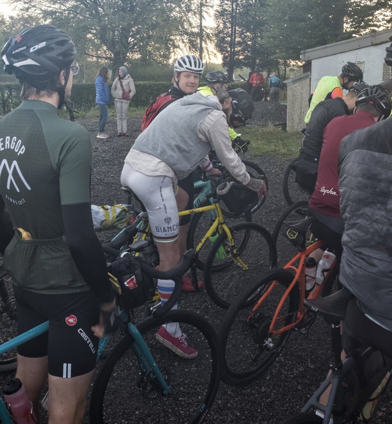 Riders stand astride their bikes waiting in a group in early morning light at the Dirty Boar.