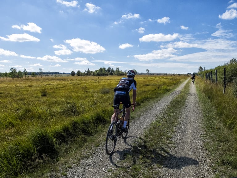 Rider on a gravel track crossing open Ardennes heathland during the Dirty Boar.