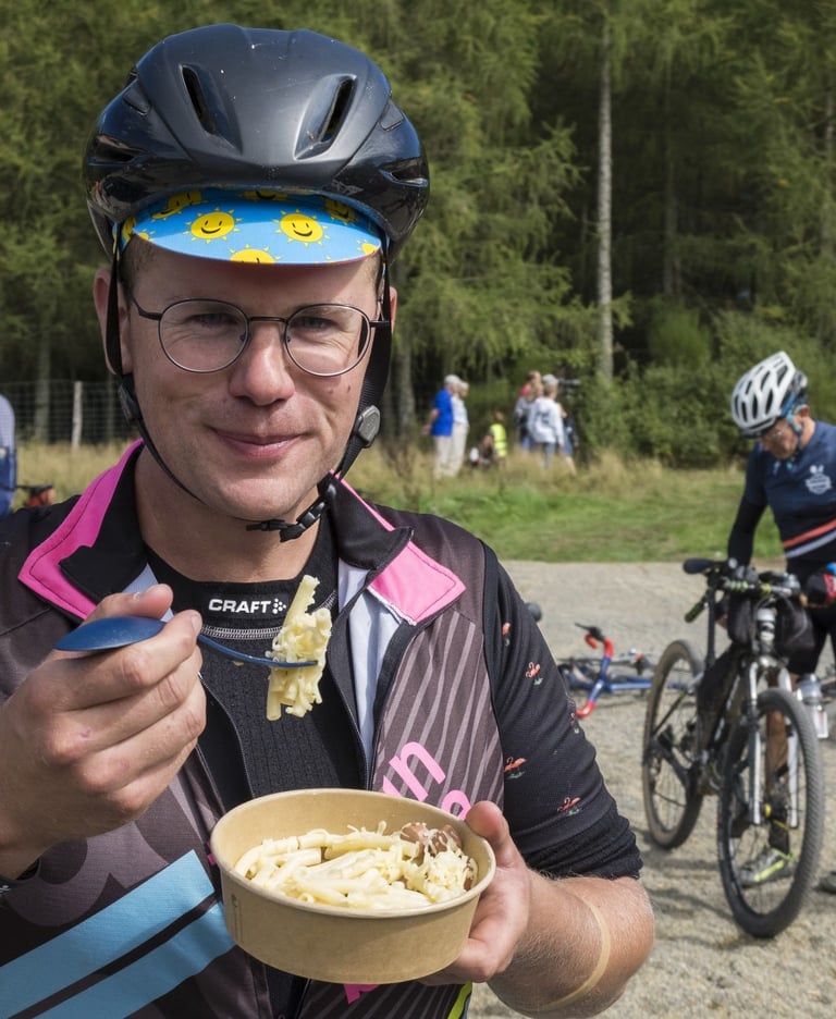 Rider in a sun-print cap eats macaroni cheese from a bowl at a Dirty Boar feed stop.