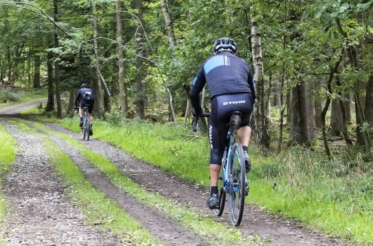 Rider in B'Twin kit on a blue gravel bike follows a grassy double-track through woodland during the Dirty Boar.