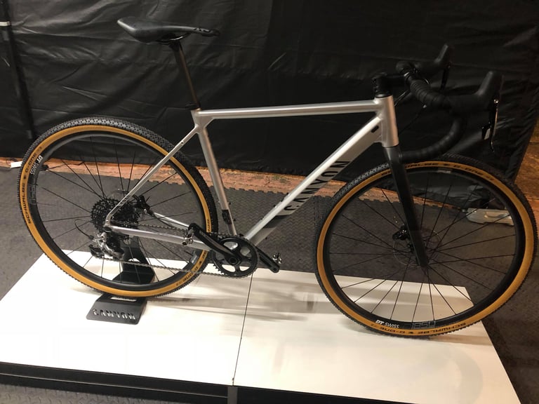 Canyon Grail AL in brushed alloy with a standard drop bar, carbon fork and SRAM 1x drivetrain on a display stand.