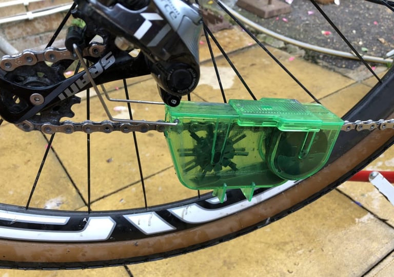 Juice Lubes Dirty Little Scrubber chain cleaner clipped onto the chain below a SRAM rear derailleur on a wet patio.