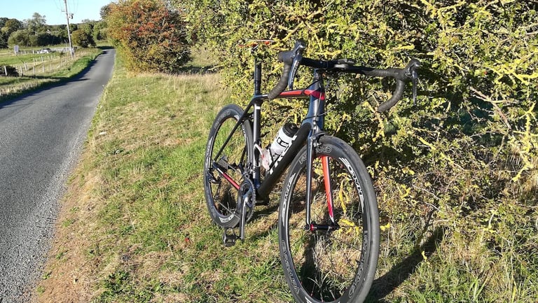 Trek Emonda with Halo Carbaura RC carbon wheels parked against a hedge beside a Suffolk country lane in low sun.