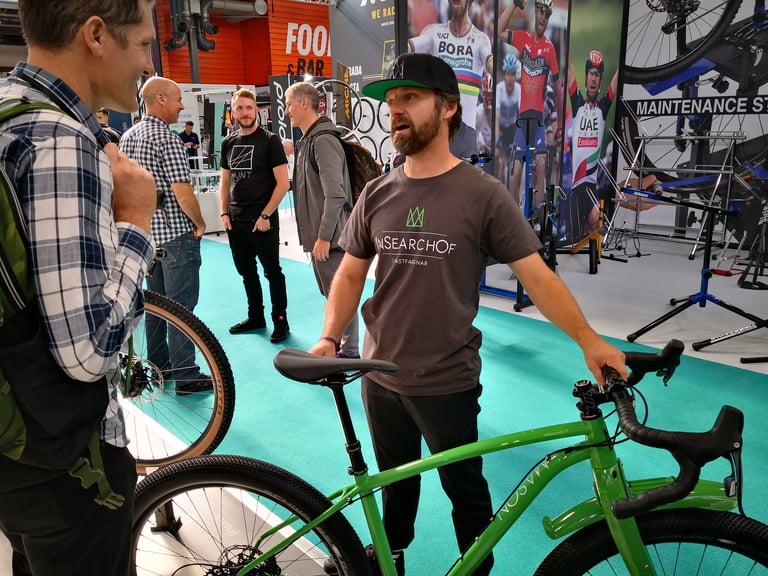 Dom Mason in an InSearchOf T-shirt stands beside the green Mason ISO at the Cycle Show, talking to visitors.