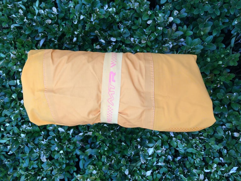 Endura MTR Shell Jacket rolled up and held by its elasticated MTR packing loop, lying on a hedge.