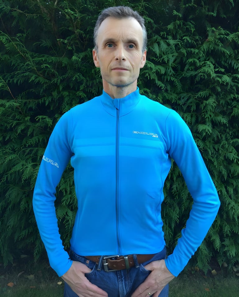 Hi Viz blue Endura Pro SL long sleeve jersey worn with jeans, full-length zip done up, in front of a conifer hedge.