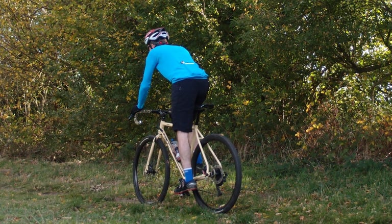 Rear view of a rider in the Endura Pro SL jersey on a cream gravel bike, on a grassy path in autumn.