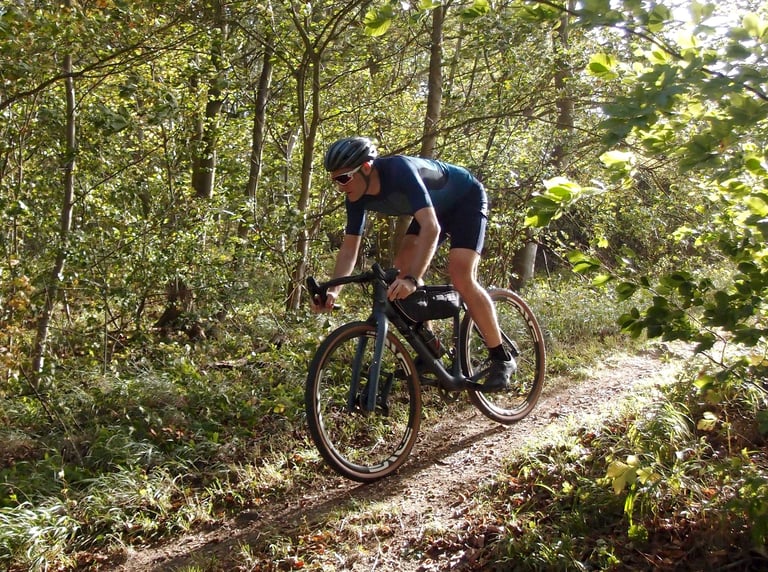 Rider on a Lauf True Grit rides a narrow woodland trail in a low, aggressive position.
