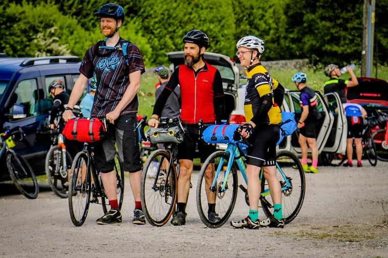 Three riders with bikepacking bags stand beside their bikes at a UK gravel ride, each in different kit.
