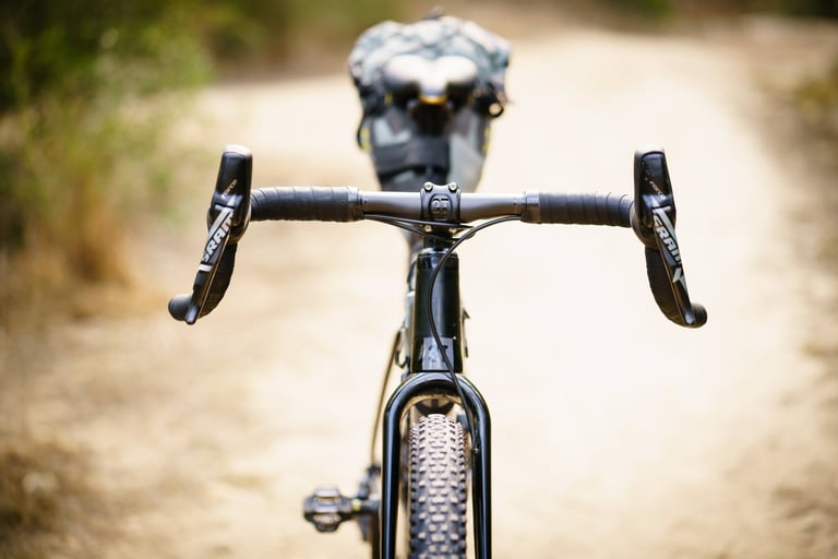 3T Superghiaia flared bars and SRAM Force levers on a bikepacking gravel bike with a saddle pack on a sandy trail.