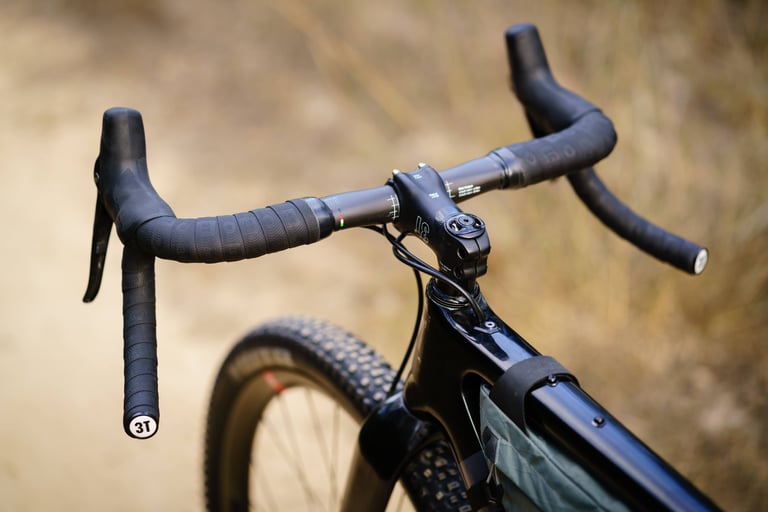 3T Superghiaia bars and stem from a raised angle, with one lever fitted, a knobbly front tyre and a frame bag below.