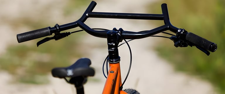 Close-up of the Surly ECR's wide swept black handlebar with grips and brake levers, orange frame below.
