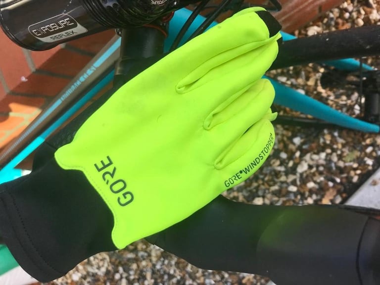 Neon yellow Gore Infinium glove, labelled Windstopper, with a long black cuff resting on a handlebar beside a teal frame.