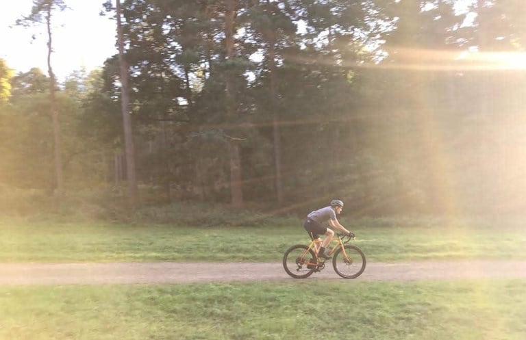 Rider on the All-City Gorilla Monsoon rolls along a gravel path through sunlit woodland.