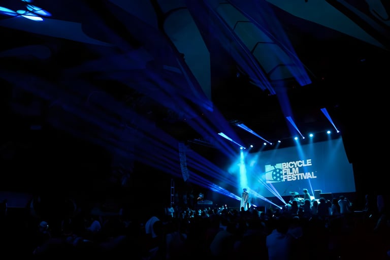 Crowd in a dark venue watching a stage under blue lights, with a Bicycle Film Festival logo on the screen.