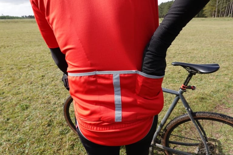 Rider's hand reaching into the rear pocket of the Le Col Therma Jersey, with a reflective strip down the back.