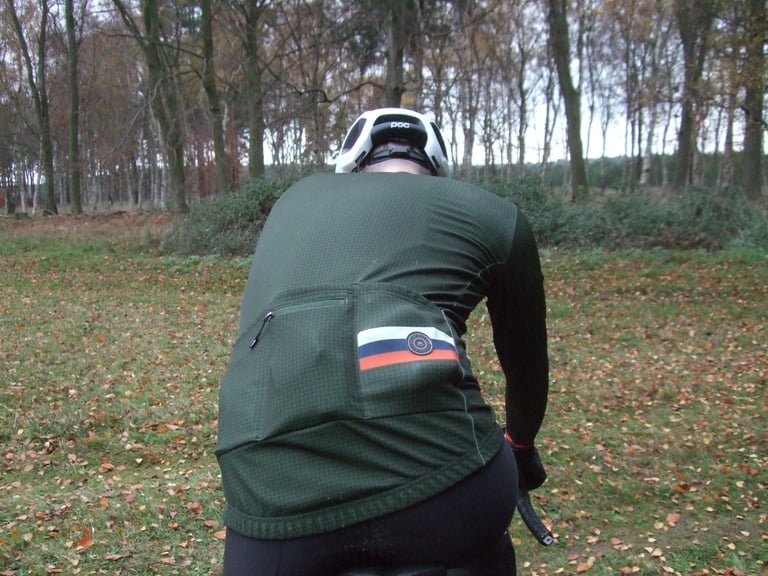 Rear view of the green Chapeau Club Thermal Jersey with its three back pockets, worn on a gravel bike.