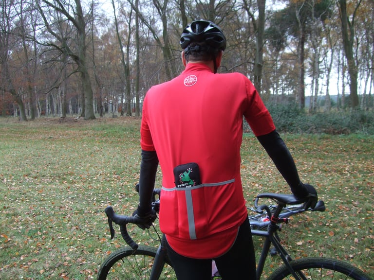 Rear of the Le Col Therma Jersey with a pouch in the loaded centre pocket, rider holding a bike in autumn woodland.