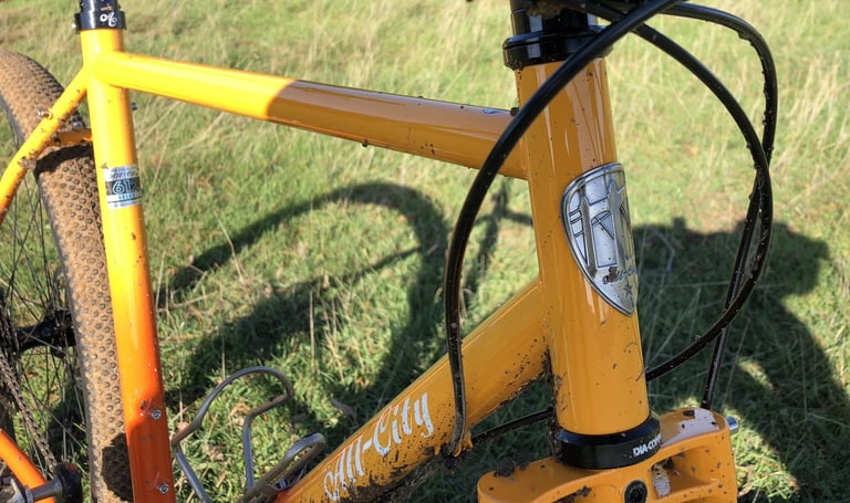 Mud-spattered head tube and badge of the All-City Gorilla Monsoon's orange steel frame.