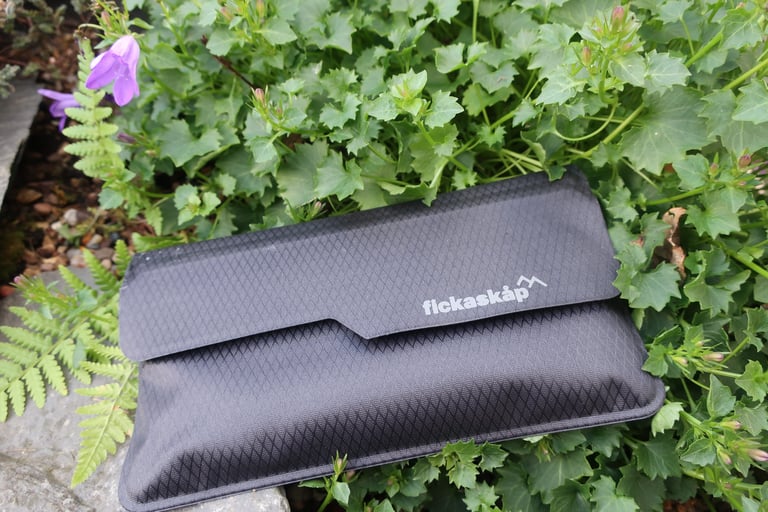 Closed black rip-stop nylon Fickaskåp wallet with its logo on the storm flap, resting on foliage.