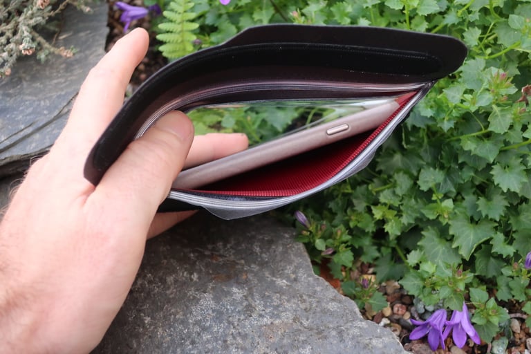 Hand holding open the Fickaskåp wallet to show a phone sealed inside its clear window with a red lining.