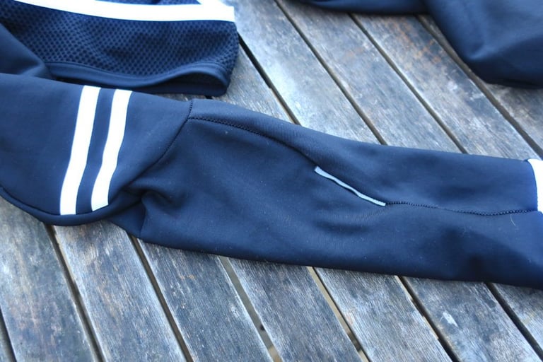 Rear of the Chapeau bibtight leg with a small reflective tab, laid on a weathered wooden table.