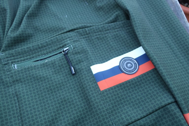 Zipped rear security pocket of the Chapeau Club Thermal Jersey with a long zip pull and striped club badge.